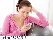 Молодая улыбающаяся брюнетка сидит с mp3 плеером, облокотившись на мяч для фитнеса. Стоковое фото, фотограф CandyBox Images / Фотобанк Лори