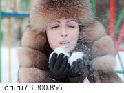 Красивая молодая женщина в меховой шапке сдувает снег с ладоней. Стоковое фото, фотограф Losevsky Pavel / Фотобанк Лори