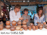 Сорочинская ярмарка. Два парня и девушка продают глиняную посуду. (2012 год). Редакционное фото, фотограф Олег Голиков / Фотобанк Лори