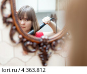Девушка смотрит на себя в зеркало и укладывает волосы плойкой. Стоковое фото, фотограф Яков Филимонов / Фотобанк Лори