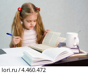 Девочка листает книгу и пишет на листе бумаги конспект сидя за столом (2013 год). Редакционное фото, фотограф Иванов Алексей / Фотобанк Лори