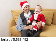 Маленький мальчик в костюме Санты сидит на коленах старенькой бабушки на диване. Стоковое фото, фотограф Андрей / Фотобанк Лори