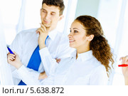 Концепция взаимодействия. Коллеги стоят у флипчарта.  Девушка пишет синим маркером, мужчина стоит рядом. Стоковое фото, фотограф Sergey Nivens / Фотобанк Лори