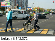 Мужчина перевозит инвалида - колясочника по пешеходному переходу. Москва, Люблинская улица (2014 год). Редакционное фото, фотограф Щеголева Ольга / Фотобанк Лори