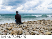 Одинокий парень сидит на каменистом берегу и смотрит на море. Стоковое фото, фотограф Ольга Визави / Фотобанк Лори