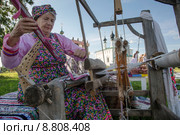 Женщина ткет на старинном станке тряпичный коврик из лоскутов ткани на фоне Входо-Иерусалимской церкви в городе Суздале. День города,  Золотое кольцо России (2015 год). Редакционное фото, фотограф Николай Винокуров / Фотобанк Лори