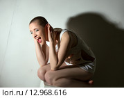 Концепция сумасшествия. Девушка в рваной белой майке сидит у белой стены. Стоковое фото, фотограф Гурьянов Андрей / Фотобанк Лори