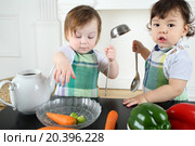 Two small children boy and girl in the kitchen apron play at a table with kitchenware and vegetables. Стоковое фото, фотограф Losevsky Pavel / Фотобанк Лори