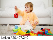 Pretty little girl sits on carpet and holds toy apple with worm at home. Shallow depth of field. Стоковое фото, фотограф Losevsky Pavel / Фотобанк Лори