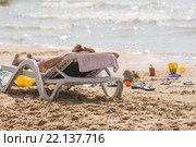 На морском пляже у воды шезлонг с загорающей девушкой, шлепки и детские игрушки для песка. Стоковое фото, фотограф Иванов Алексей / Фотобанк Лори