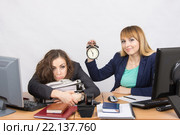 Две девушки в офисе в конце рабочего дня, одна с улыбкой держит часы, другая утомленно лежит на папках. Стоковое фото, фотограф Иванов Алексей / Фотобанк Лори