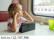 Девочка задумавшись посмотрела в окно сидя с планшетом в вагоне поезда. Стоковое фото, фотограф Иванов Алексей / Фотобанк Лори
