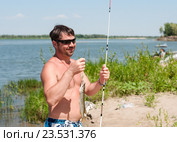 Рыбак с пойманной на блесну щукой и спиннингом на фоне реки. Стоковое фото, фотограф Игорь Низов / Фотобанк Лори