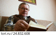 Old man sitting on the couch at home reading a book. Стоковое видео, видеограф Сергей Кальсин / Фотобанк Лори