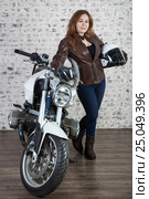 Attractive woman in vintage outfit holds white helmet, standing near motorcycle, brick wall background. Стоковое фото, фотограф Кекяляйнен Андрей / Фотобанк Лори