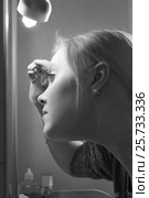A young girl plucks eyebrows in front of the mirror, black and white. Стоковое фото, фотограф Юлия Юриева / Фотобанк Лори