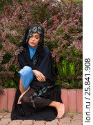 Sad woman in black sari sitting at border under bushes of barberry in park. Стоковое фото, фотограф Losevsky Pavel / Фотобанк Лори
