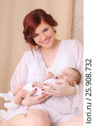 Happy young mother in a white silk dress, holds her baby in her arms and smiling. Стоковое фото, фотограф Светлана Додух / Фотобанк Лори