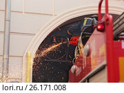 Пожарный болгаркой спиливает металлическую решетку, мешающую проезду пожарной машины (2017 год). Редакционное фото, фотограф Юрий Кирсанов / Фотобанк Лори