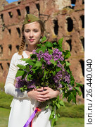 A young girl in a second world war epoch head-dress holding a lilac bouquet against the demolished building background. Стоковое фото, фотограф Макалиш Андрей / Фотобанк Лори