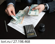 Руководитель предприятия подсчитывает деньги для оплаты налога на фоне декларации на вменённый доход. Стоковое фото, фотограф Игорь Низов / Фотобанк Лори