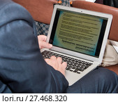 Мужчина работает на ноутбуке, лежащем на коленях. На экране приведена информация по проблематике законотворческого документооборота (2014 год). Редакционное фото, фотограф Наталья Николаева / Фотобанк Лори
