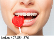 Woman bites off red lollipop in the shape of heart. Стоковое фото, фотограф Сергей Новиков / Фотобанк Лори