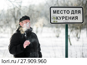 Мужчина курит сигарету возле таблички "Место для курения" морозным днём. Стоковое фото, фотограф Игорь Низов / Фотобанк Лори