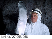 Speleologist in a cave examines a giant ice stalagmite covered with hoarfrost, against a background of a dark rock covered with ice crystals. Стоковое фото, фотограф Евгений Харитонов / Фотобанк Лори