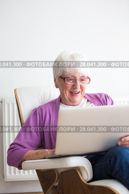 Portrait of a senior woman at home - Laughing at something on her laptop computer, sitting in her favorite chair, enjoying retirement. Стоковое фото, фотограф Viktor Cap / PantherMedia / Фотобанк Лори