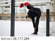 Man in black does stretching exercises on sport playground near building at winter. Стоковое фото, фотограф Losevsky Pavel / Фотобанк Лори