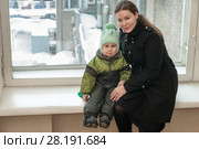 Mother and little child sitting in warm clothes on window sill inside the hall. Стоковое фото, фотограф Кекяляйнен Андрей / Фотобанк Лори