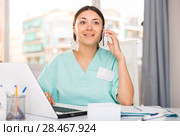 Practicioner woman in medical uniform talking by phone at laptop. Стоковое фото, фотограф Яков Филимонов / Фотобанк Лори