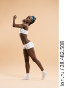 Full-length portrait of a sporty young cheerful african woman standing on beige background. Стоковое фото, агентство Ingram Publishing / Фотобанк Лори