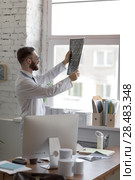 Closeup portrait of intellectual man healthcare personnel with white labcoat, looking at brain x-ray radiographic image, ct scan, mri, clinic office background. Radiology department. Стоковое фото, агентство Ingram Publishing / Фотобанк Лори