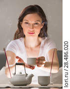 Young woman sitting in meditation pose in front of tea set and aroma sticks. Relaxation concept. Стоковое фото, фотограф Kirill Kedrinskiy / Ingram Publishing / Фотобанк Лори