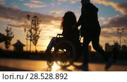 Caring man with a disabled woman in wheelchair walking through the quay at sunset. Стоковое видео, видеограф Константин Шишкин / Фотобанк Лори