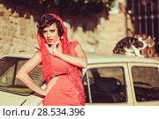Portrait of a pretty woman, vintage style, in urban background, wearing a red dress, with a old car and a cat. Стоковое фото, фотограф Javier Sánchez Mingorance / Ingram Publishing / Фотобанк Лори