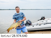 Счастливый рыбак с сазаном в руках на фоне реки (2018 год). Редакционное фото, фотограф Игорь Низов / Фотобанк Лори