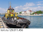 Sea tug at the pier. Russia, the peninsula of Crimea, the city of Sevastopol. 06/10/2018: Sea tugboat "Sevastopolets" at the pier in the Artillery Bay. View of the Kornilov Embankment and Primorsky Boulevard. Редакционное фото, фотограф Вадим Орлов / Фотобанк Лори