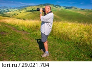 Фотограф снимает горный пейзаж Алтая, поднявшись на высокий холм. Район реки Малый Каим, Горный Алтай, Южная Сибирь, Россия (2018 год). Редакционное фото, фотограф Евгений Мухортов / Фотобанк Лори