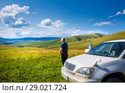 Автотурист смотрит на холмы и горы Алтая, поднявшись на высокий холм. Район реки Малый Каим, Горный Алтай, Южная Сибирь, Россия (2018 год). Редакционное фото, фотограф Евгений Мухортов / Фотобанк Лори