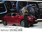 Московский автосалон 2018 года, девушка модель у красного автомобиля KIA на фоне большого руля. Редакционное фото, фотограф Дмитрий Неумоин / Фотобанк Лори