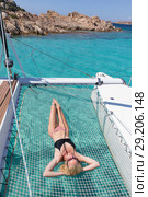 Woman relaxing on a summer sailing cruise,lying in hammock of luxury catamaran near picture perfect white sandy beach on Spargi island in Maddalena Archipelago, Sardinia, Italy. Стоковое фото, фотограф Matej Kastelic / Фотобанк Лори