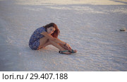 Calm girl enjoying sun, sits on the ground covered with salt close to lake. Стоковое видео, видеограф Ирина Мойсеева / Фотобанк Лори