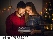 Парень дарит девушке новогодний подарок на фоне новогодних украшений. Стоковое фото, фотограф Никита Биржаков / Фотобанк Лори