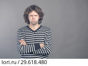 Angry young man in striped sweater puffed up his cheeks and crossed arms about to have nervous breakdown, isolated on gray wall background. Negative human emotions facial expression feelings attitude. Стоковое фото, фотограф Marina Sharova / Фотобанк Лори