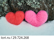 Two woolen red and pink hearts standing on the white snow near a tree trunk. Стоковое фото, фотограф Георгий Дзюра / Фотобанк Лори