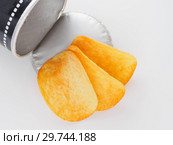 Crispy potato chips are poured out of the package in the form of a cardboard tube / cylinder on white background. Стоковое фото, фотограф Евгений Бобков / Фотобанк Лори