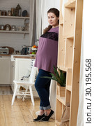 Pregnant European woman standing in kitchen, looking at camera, full length portrait. Стоковое фото, фотограф Кекяляйнен Андрей / Фотобанк Лори